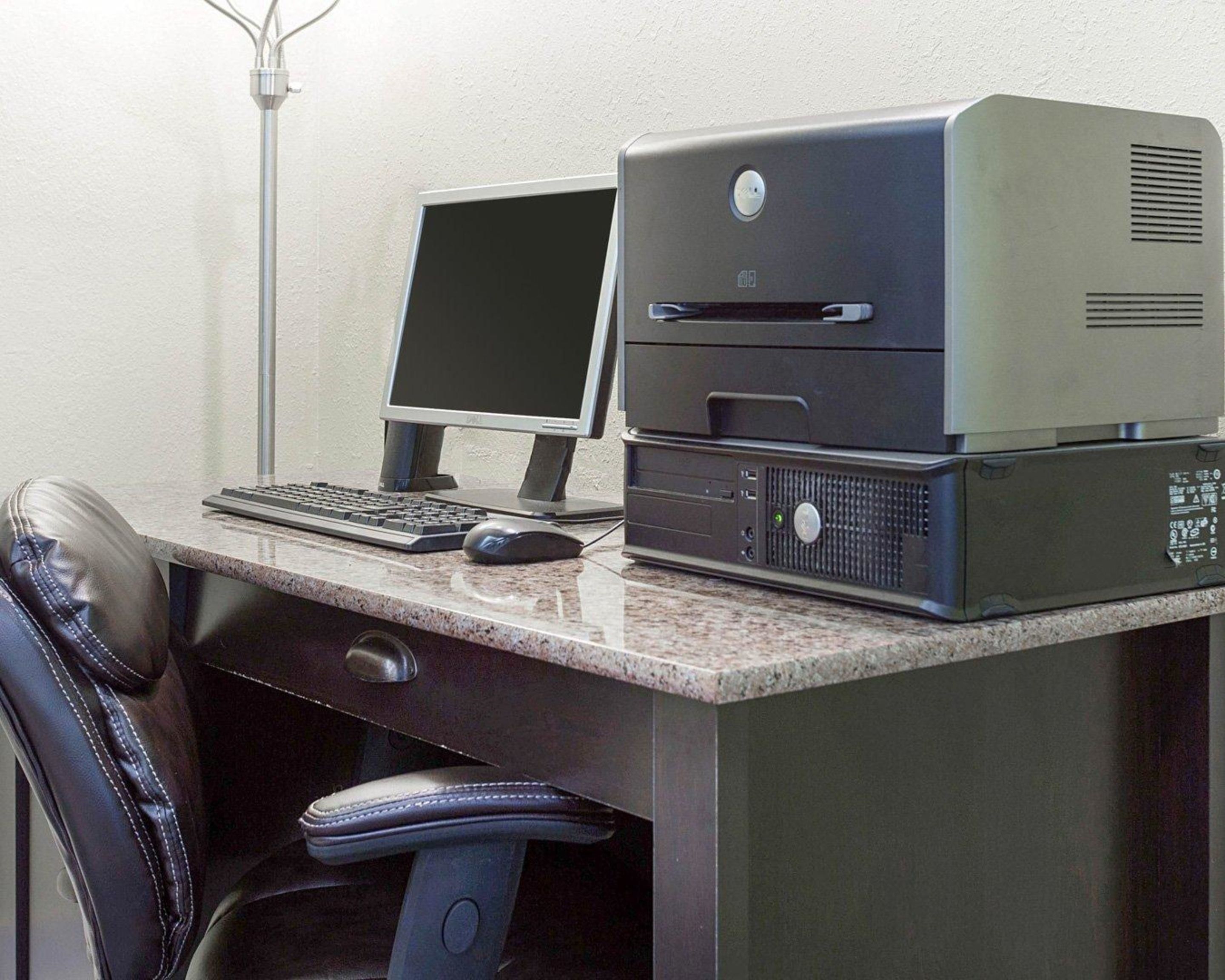 A desktop computer with a monitor and printer on a desk, a keyboard, a mouse, and a chair.