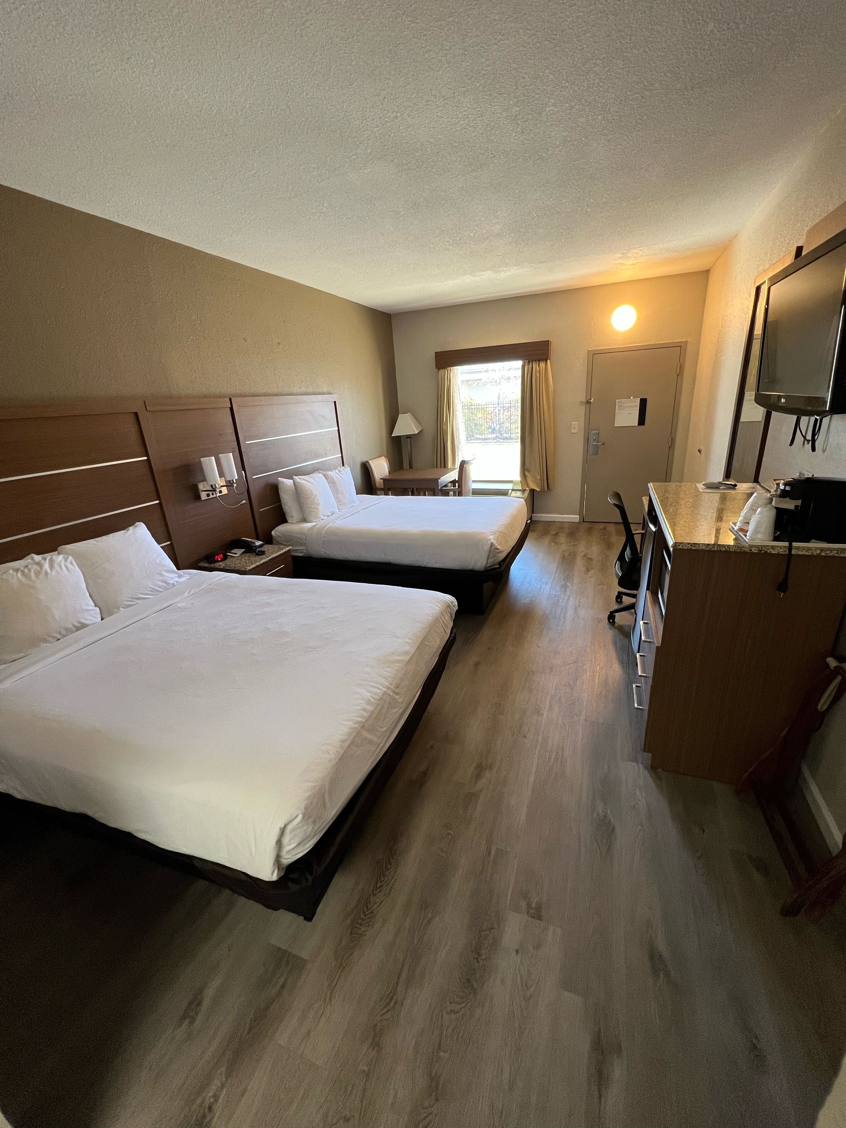 A hotel room with two beds, a desk, a TV, and a window with curtains.