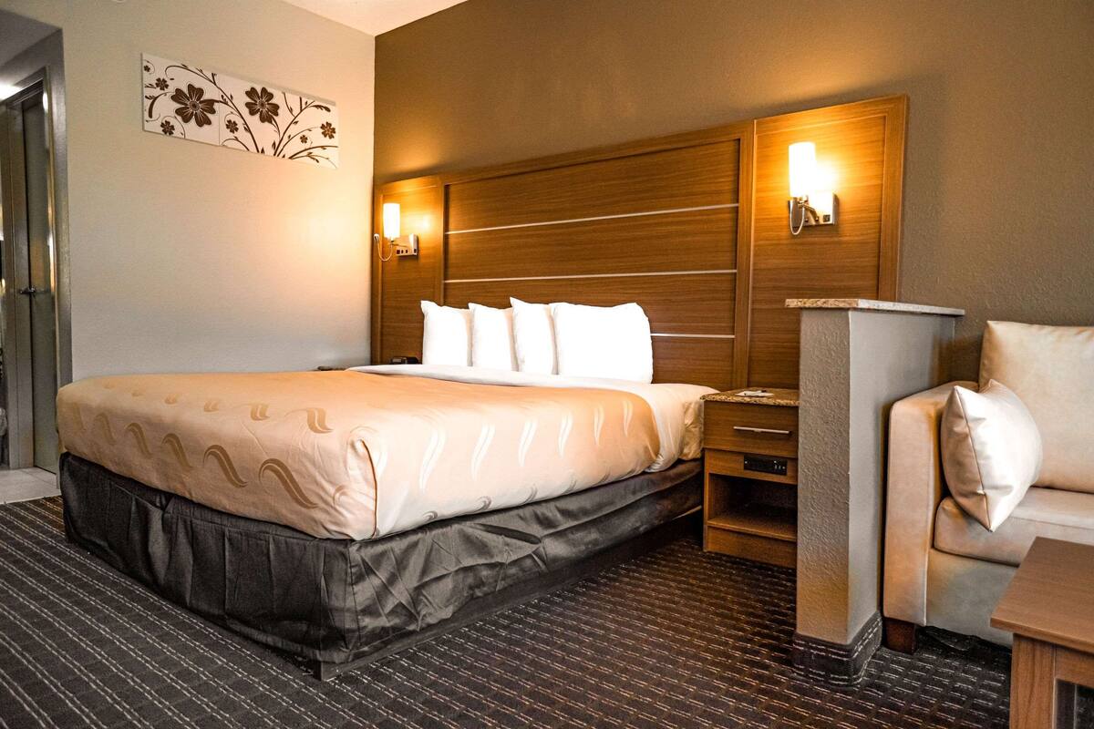A hotel room with a large bed, a wooden headboard, two wall-mounted lights, a small table, and a sofa.