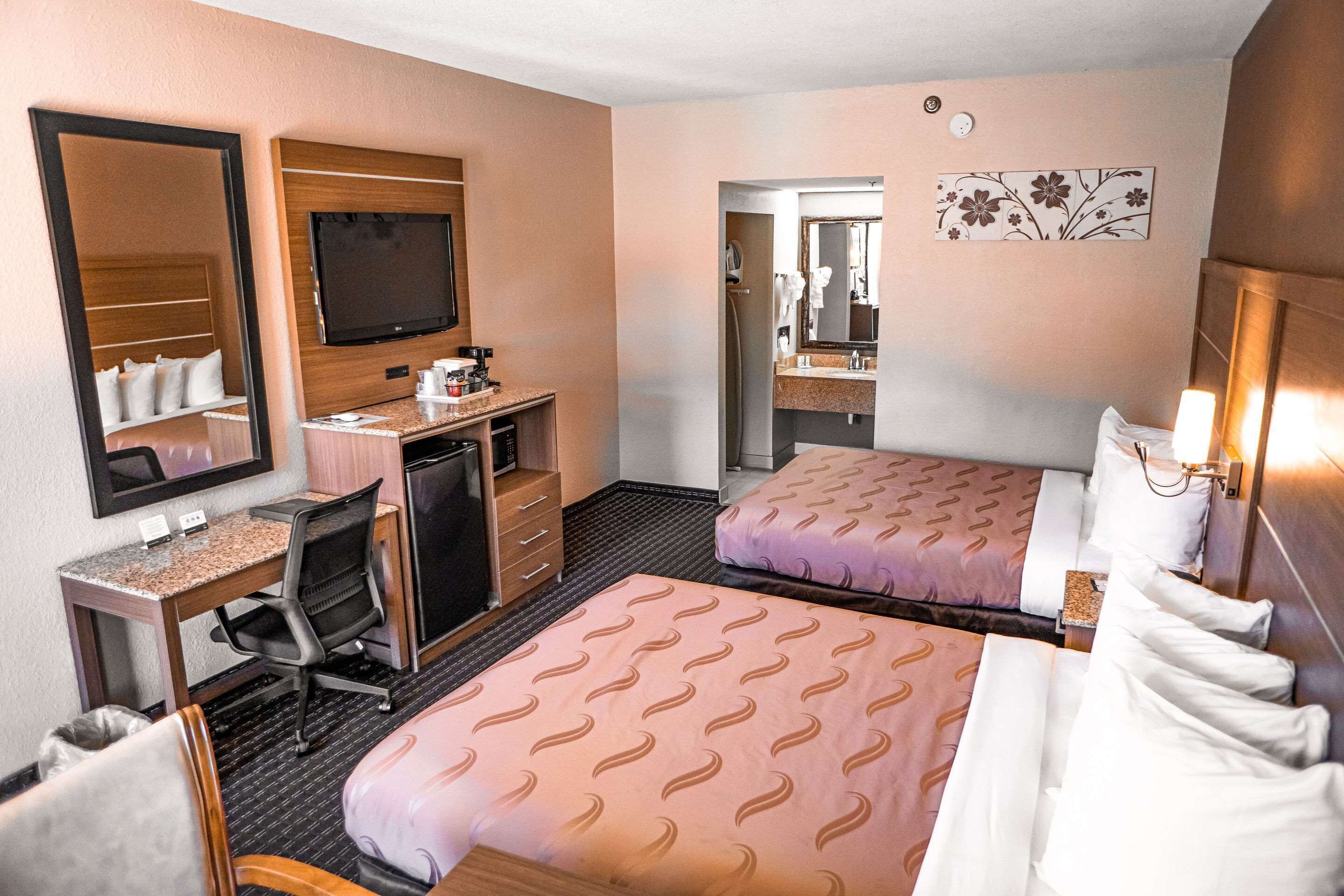 A hotel room with two beds, a desk with a computer, a TV, and a mirror.