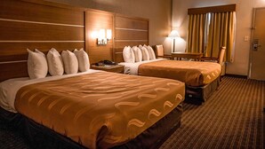 Een hotelkamer met twee bedden, een bureau, een stoel, een lamp en een raam met gordijnen.