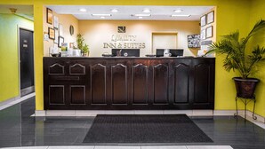 Een receptiebalie met een bordje waarop 'Quality Inn & Suites' staat, een computer en een potplant.