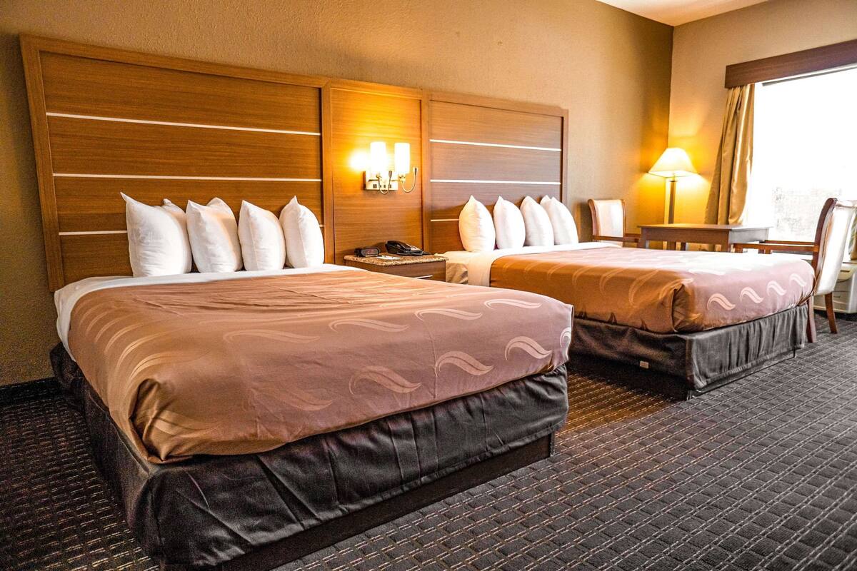 A hotel room with two beds, a desk, a chair, and a window.