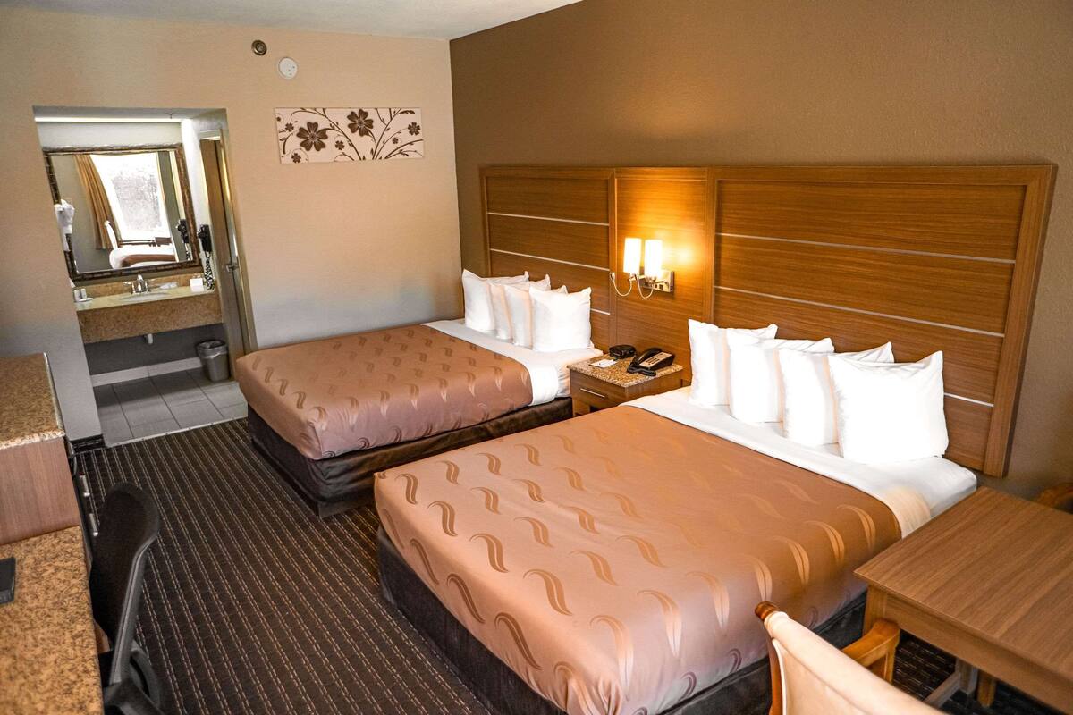 A hotel room with two beds, a bedside table with a lamp, a mirror, and a small desk with a telephone.
