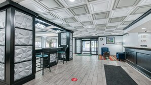 Un hall d’hôtel moderne avec un mur orné de motifs géométriques, un comptoir d’accueil, un bar et un espace détente avec des sièges.