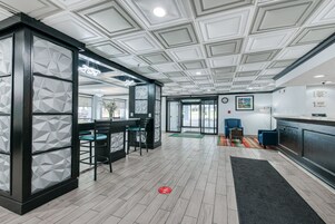 Un vestíbulo moderno de hotel con un muro de diseño geométrico, una recepción, una zona de bar y asientos.