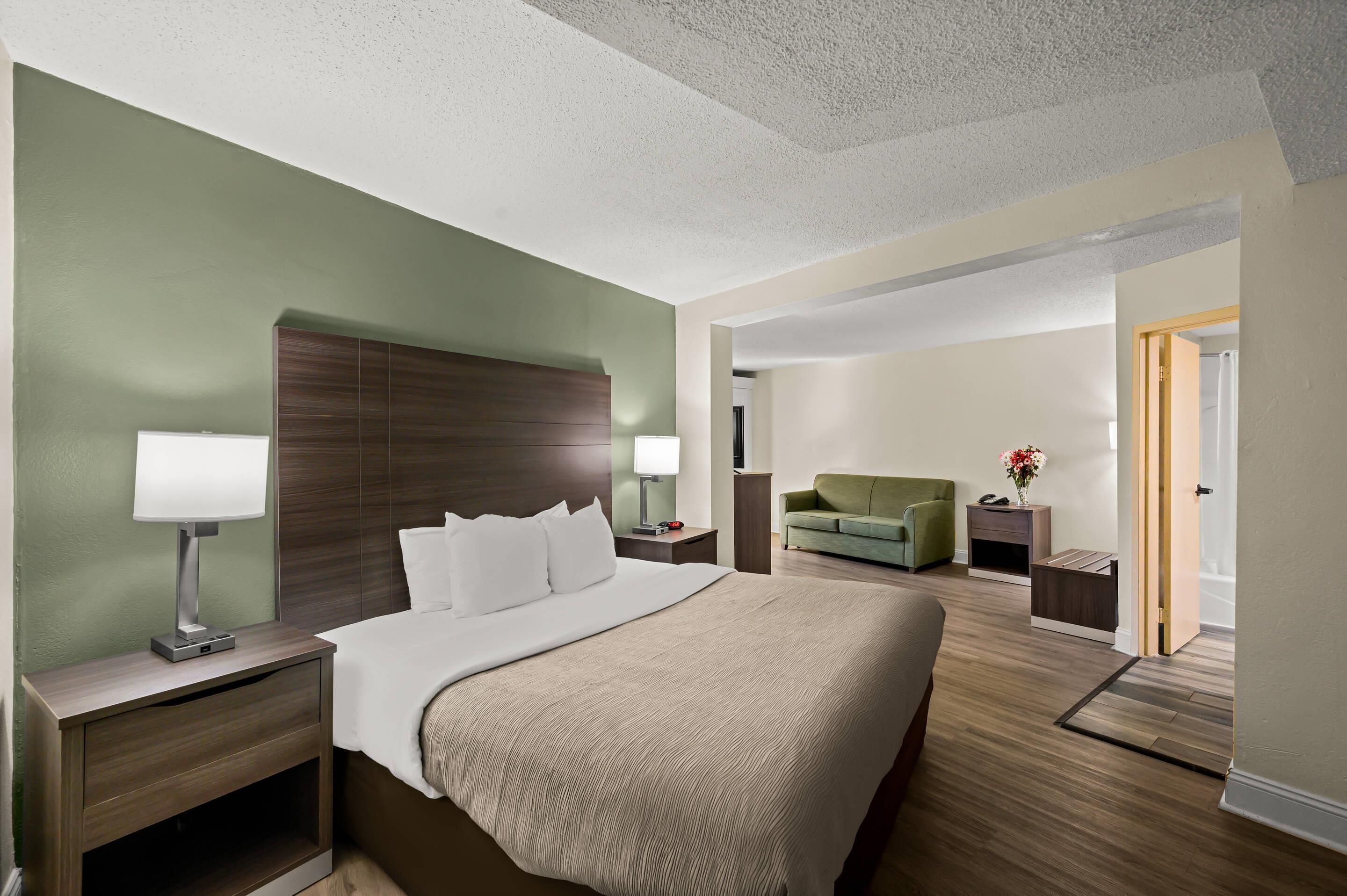 Quarto de hotel com uma cama grande, mesas de cabeceira, escrivaninha, uma cadeira e porta para o banheiro.