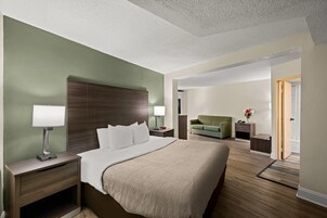 Habitación de hotel con una cama grande, mesitas de noche, un escritorio, una silla y una puerta que da al baño.