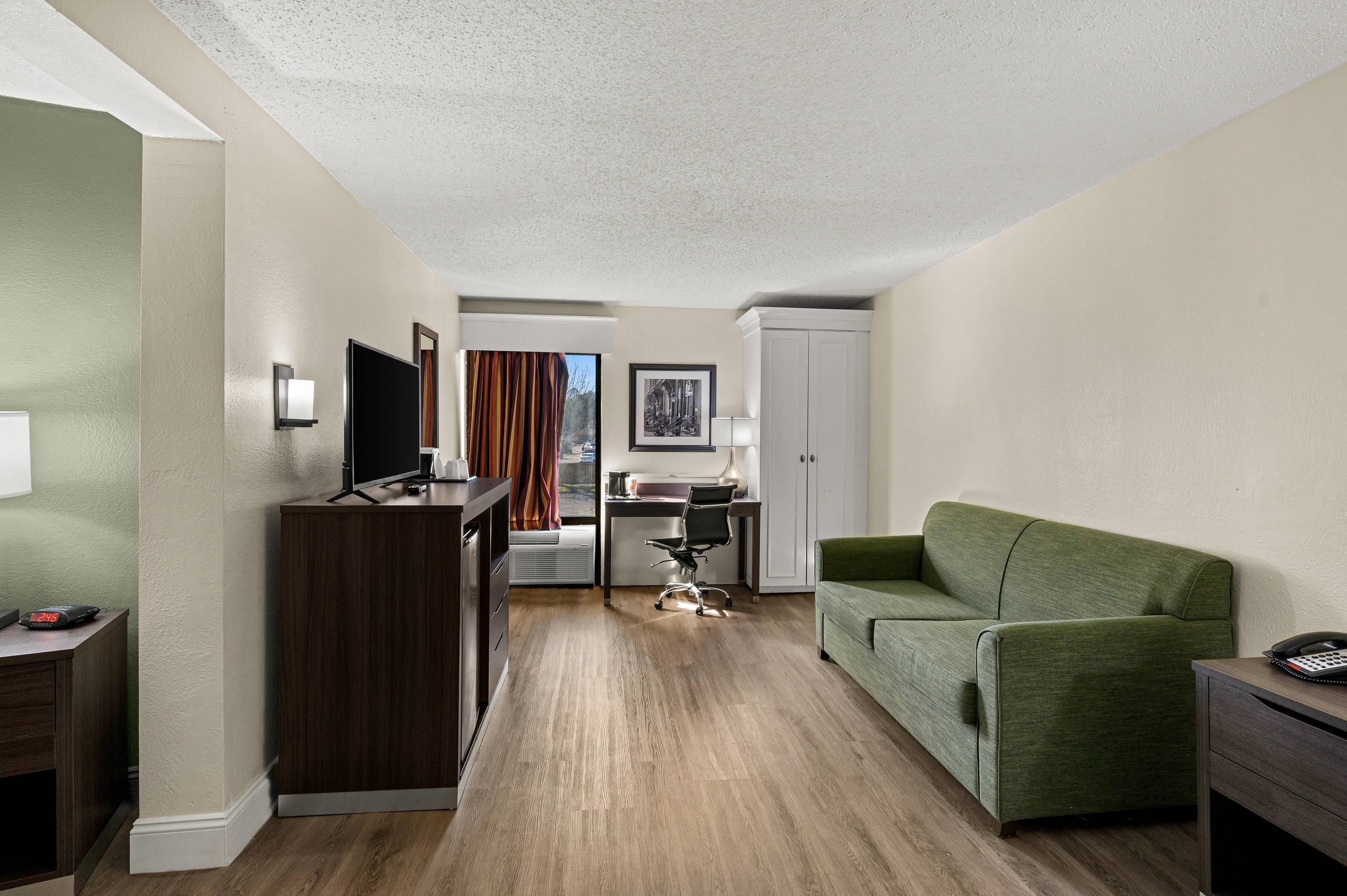 Hotelkamer met houten vloer, een groene bank, een bureau met stoel, een televisie en een kledingkast.