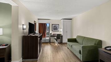 Hotelkamer met houten vloer, een groene bank, een bureau met stoel, een televisie en een kledingkast.