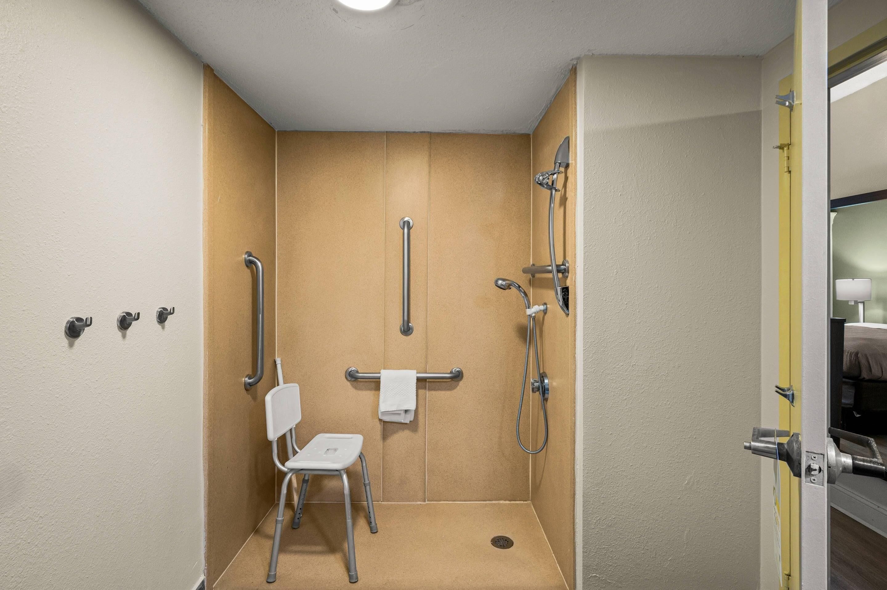 A small, enclosed shower area with a chair, grab bars, and a towel rack.