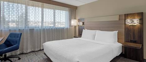 Une chambre d’hôtel avec un grand lit, un bureau, une chaise et une fenêtre avec des rideaux à motifs.