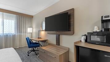 A hotel room with a bed, a desk with a chair, a television, a coffee maker, and a microwave.
