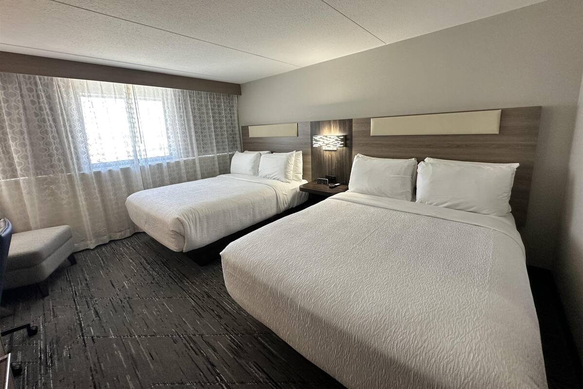 Een hotelkamer met twee bedden, een nachtkastje met een lamp, een stoel en een raam met gordijnen.