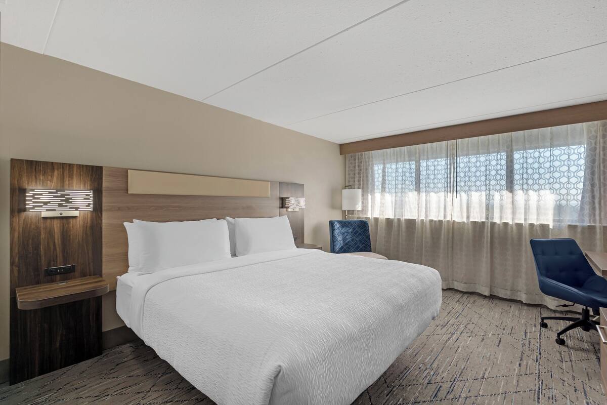 Een hotelkamer met een groot bed, een bureau, een stoel en een raam met gordijnen.