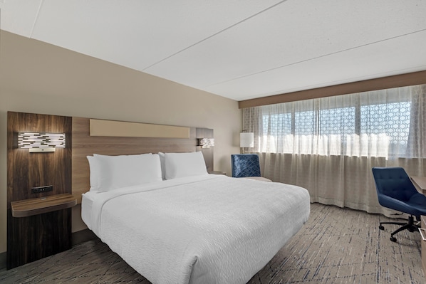 A hotel room with a large bed, a desk, a chair, and a window with curtains.