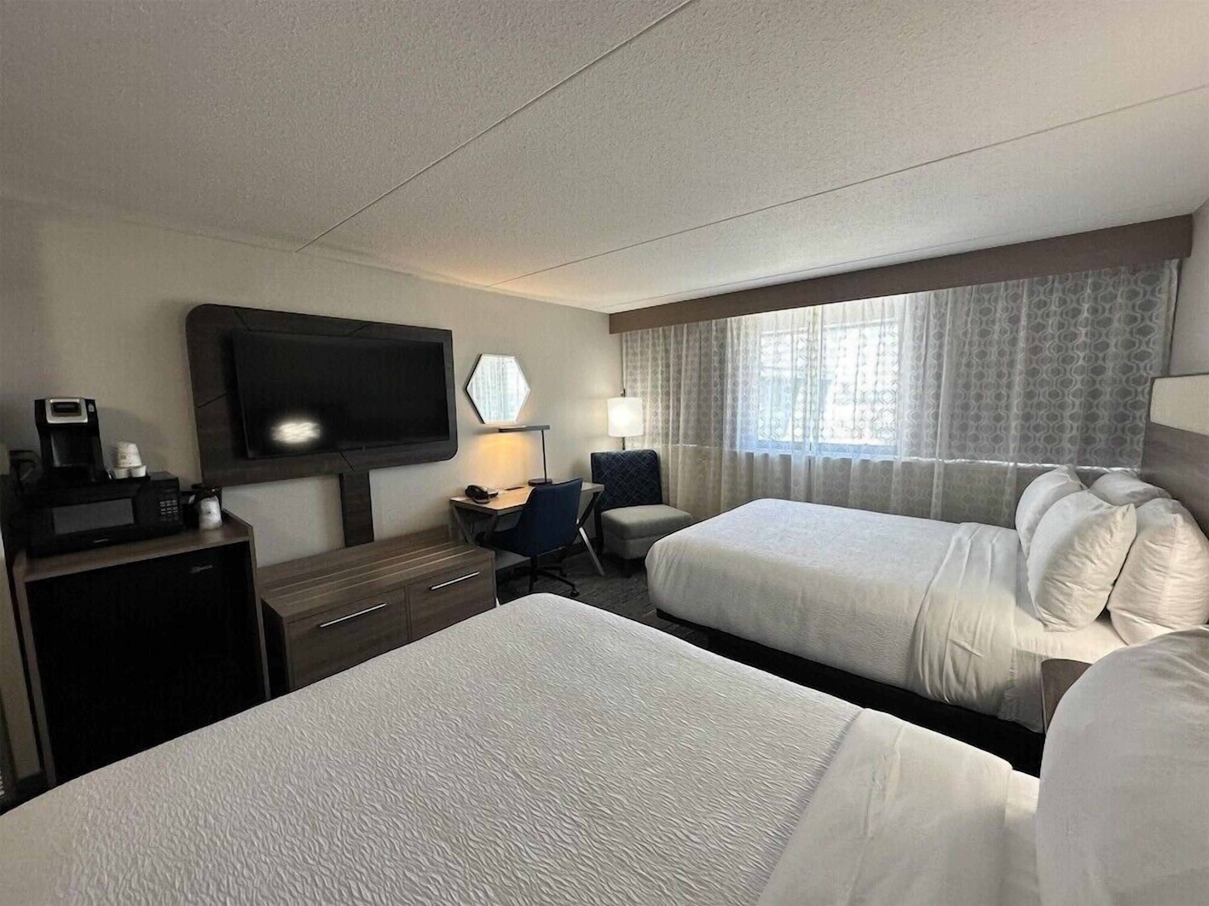 A hotel room with two beds, a desk with a chair, a television, and a window with curtains.