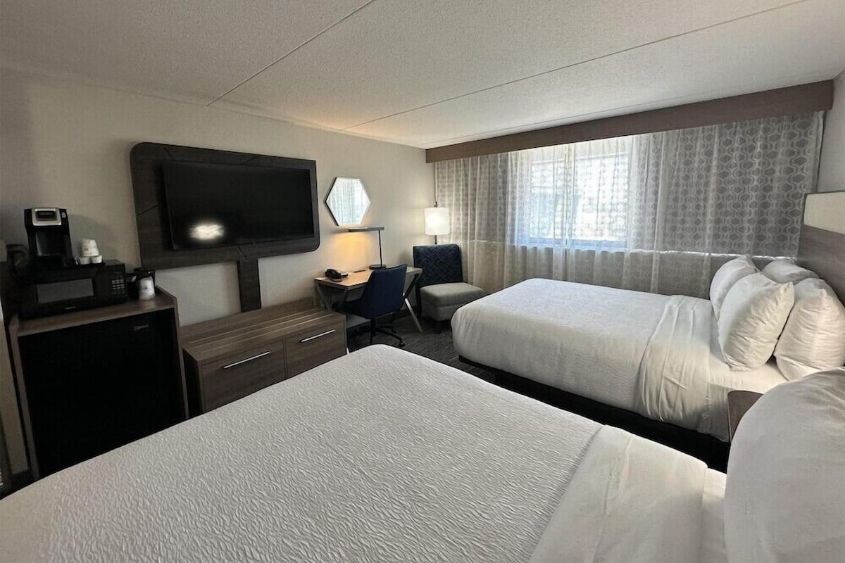 A hotel room with two beds, a desk with a chair, a television, and a window with curtains.