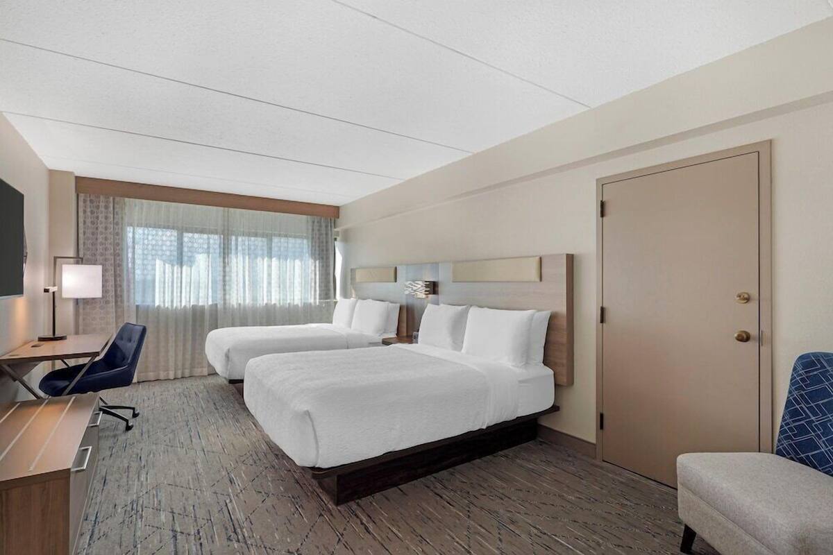 Een hotelkamer met twee bedden, een bureau, een stoel, een kledingkast en een raam met gordijnen.