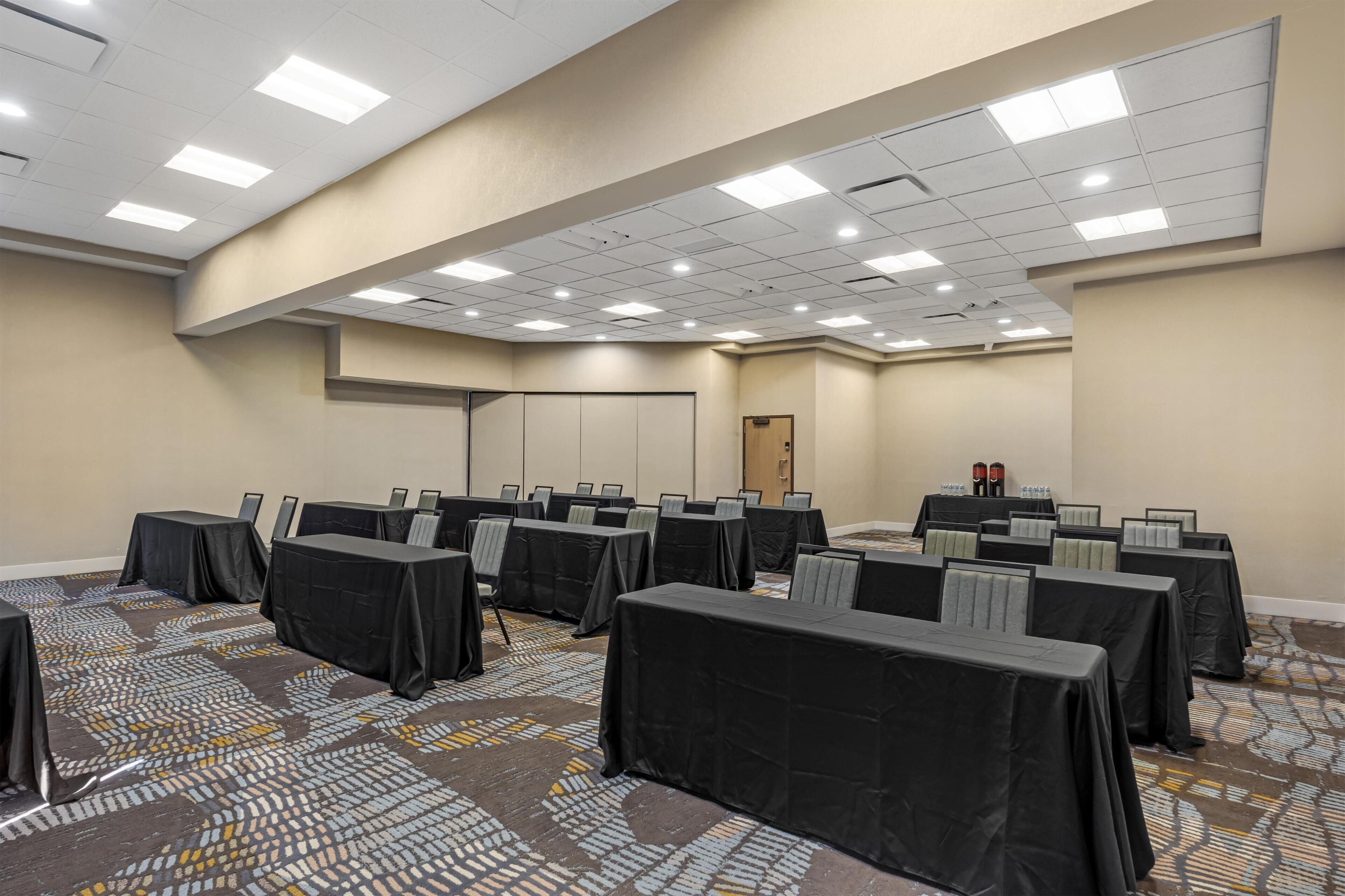 A conference room with multiple tables, chairs, and a patterned carpet.