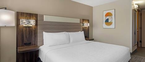 A hotel room with a large bed, wooden headboard, two bedside tables with lamps, a wall-mounted artwork, and a carpeted floor.