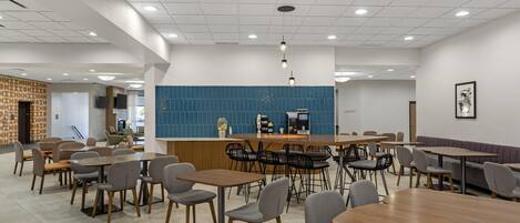 A modern dining area with multiple tables and chairs, a central bar, and a blue-tiled wall.