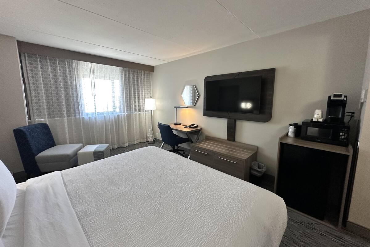 Een hotelkamer met een bed, bureau, stoel, televisie en koffiezetapparaat.