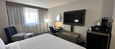 A hotel room with a bed, a desk, a chair, a television, and a coffee maker.