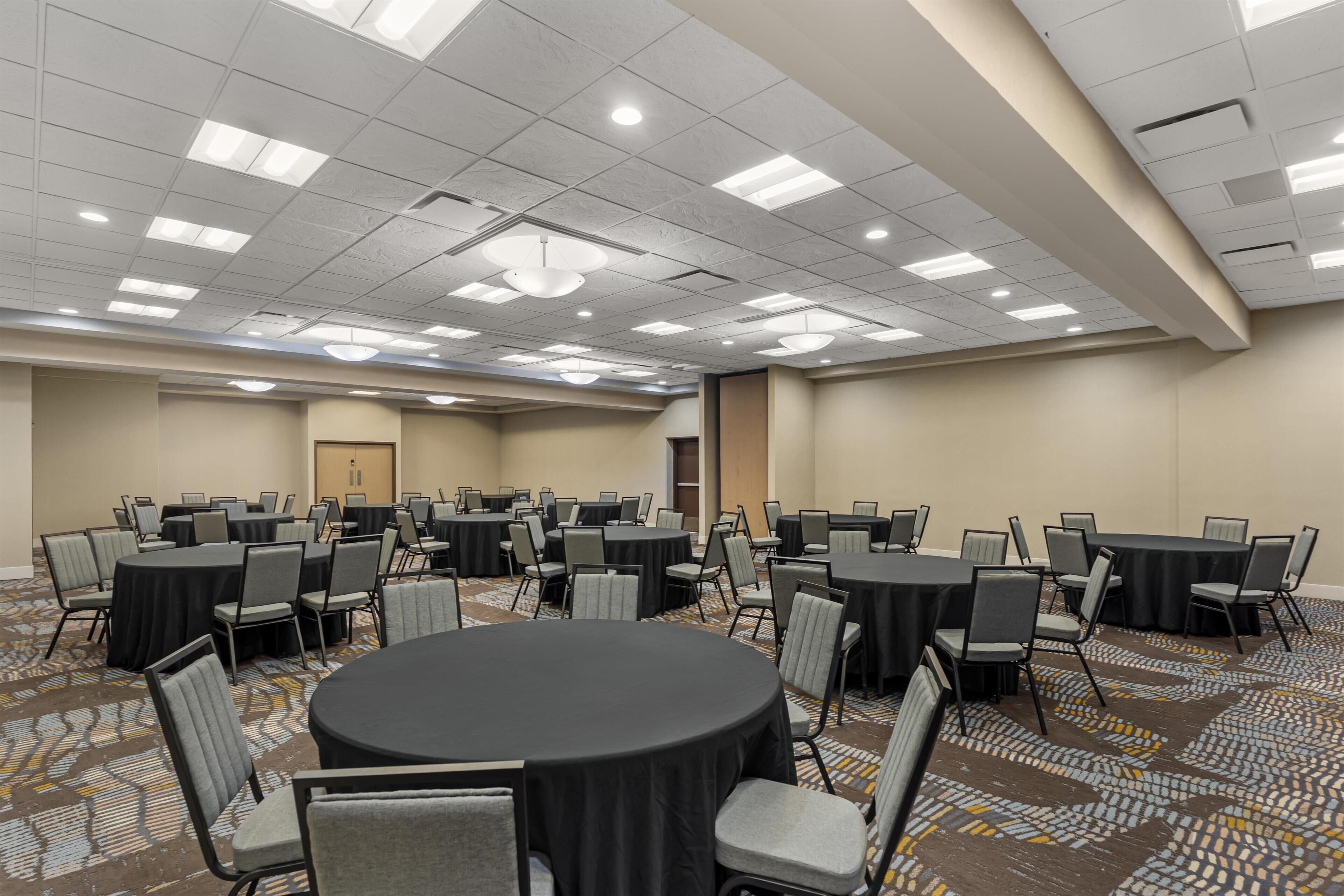 A conference room with multiple tables and chairs, a patterned carpet, and a ceiling with recessed lighting.