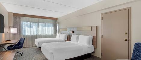 A hotel room with two beds, a desk, a chair, a TV, and a wardrobe.
