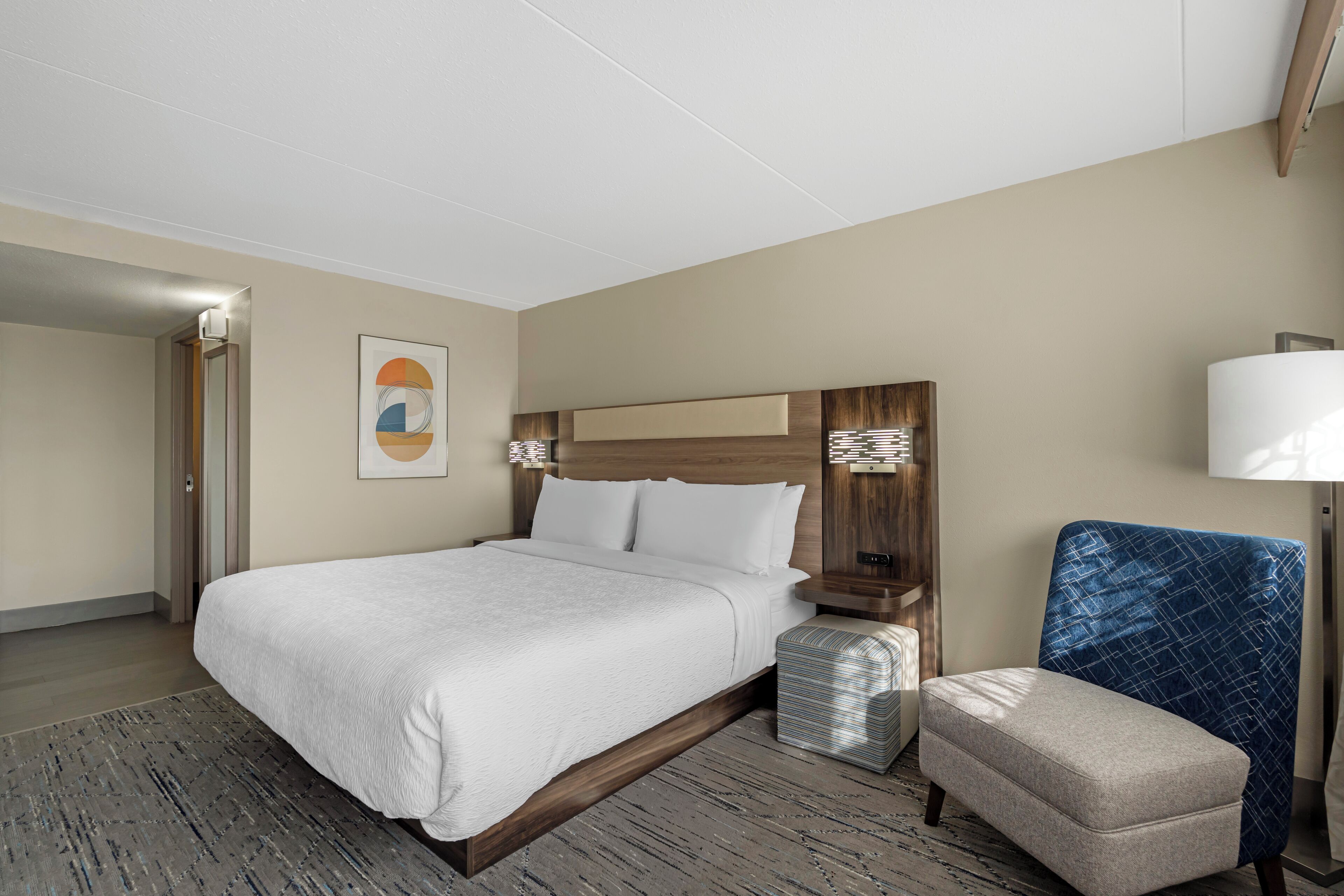 A hotel room with a large bed, a nightstand, a chair, and a lamp.