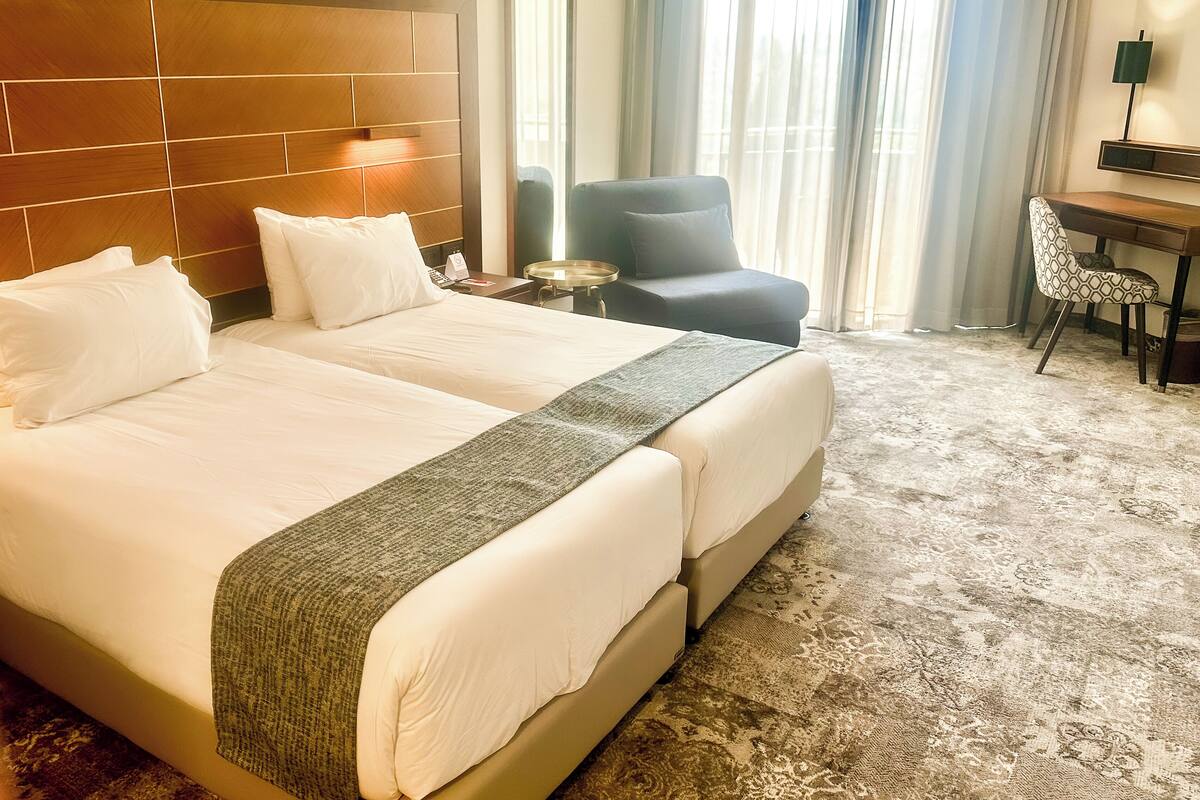 Quarto de hotel com uma cama grande, uma escrivaninha, uma cadeira e uma janela com cortinas.
