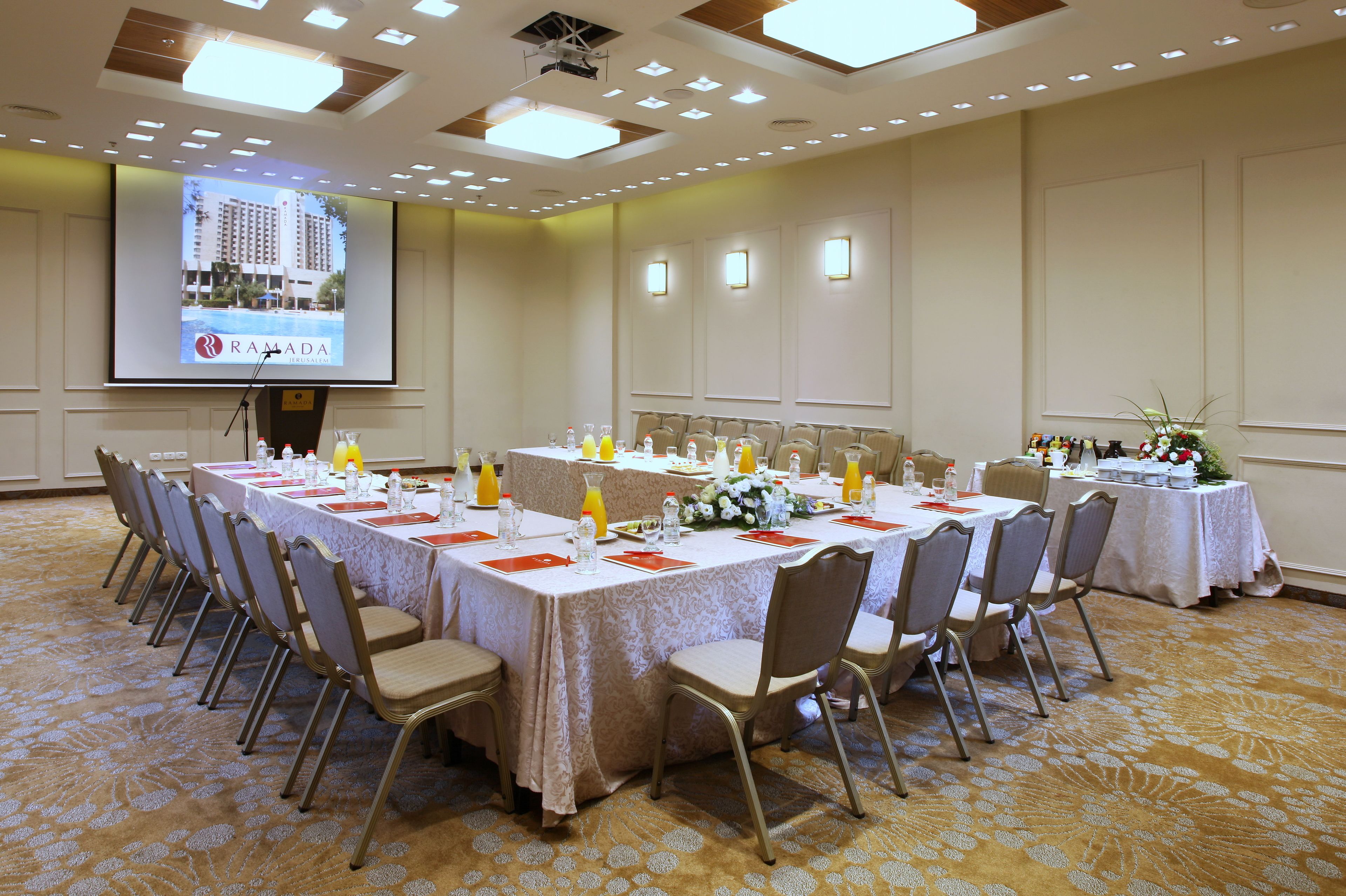A conference room with multiple tables set for a meeting, equipped with chairs, water bottles, and floral centerpieces.