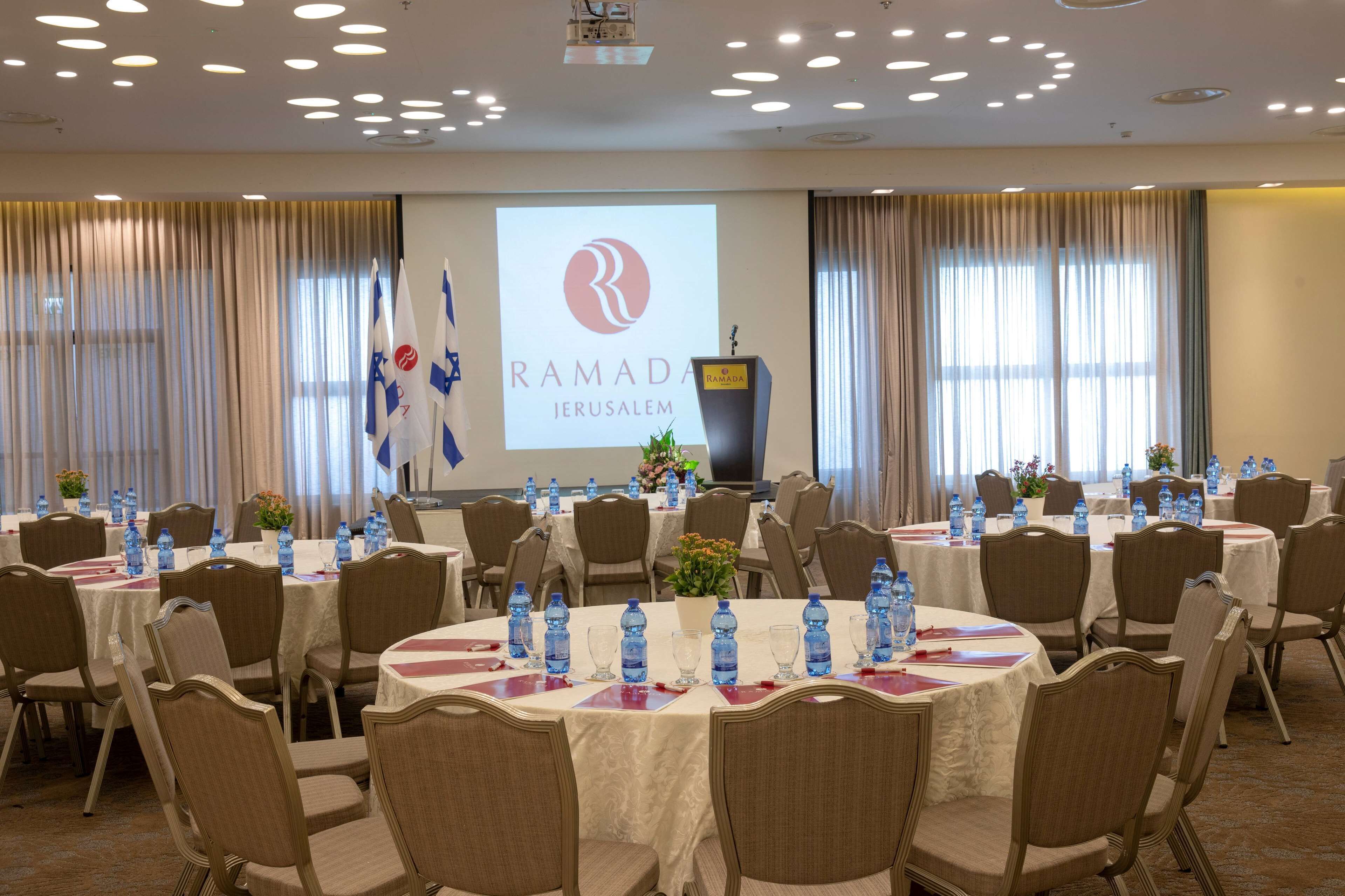 A conference room with round tables, chairs, and a projector screen displaying the Ramada Jerusalem logo.