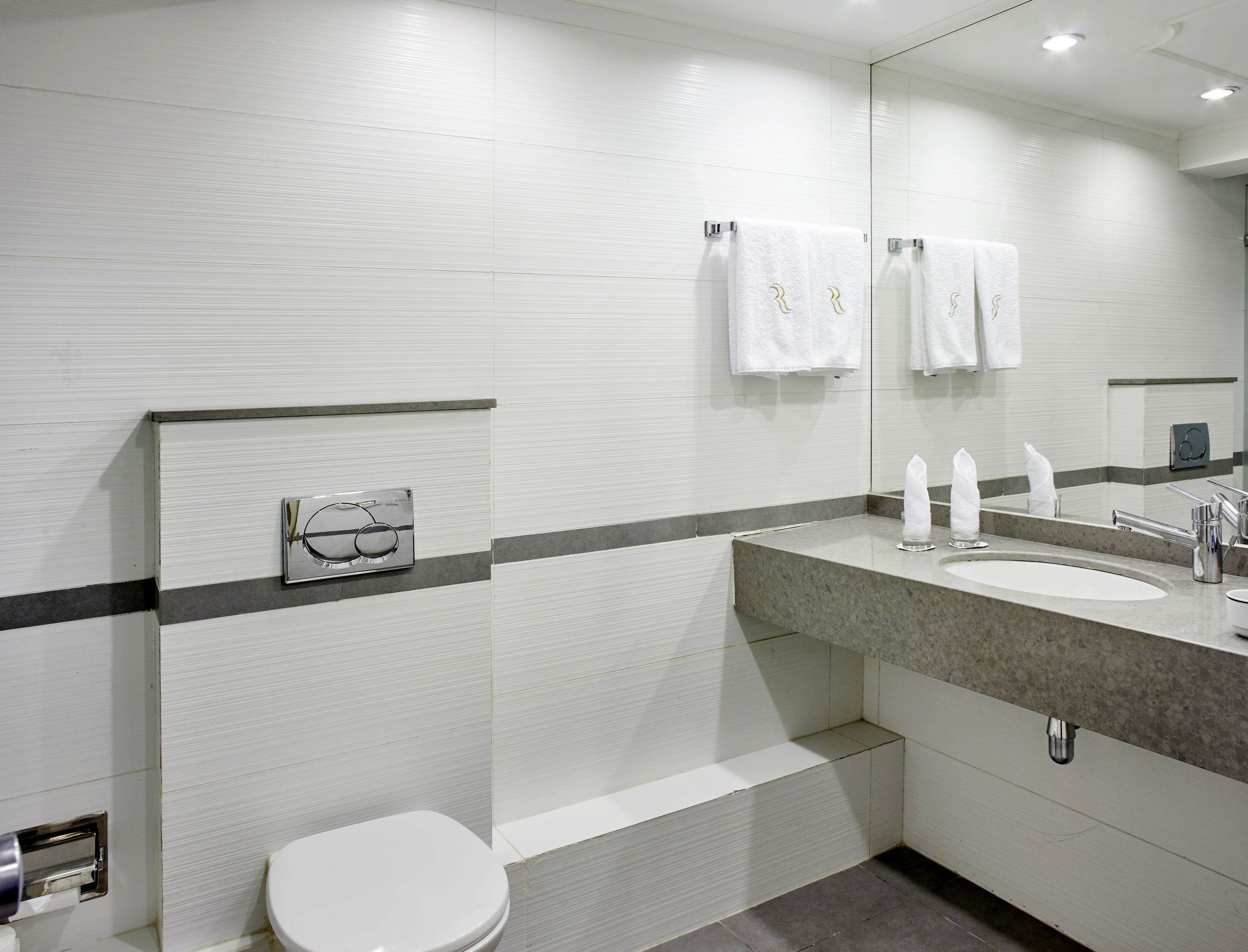 Un baño moderno con inodoro blanco, lavabo con espejo y toallas colgadas en la pared.