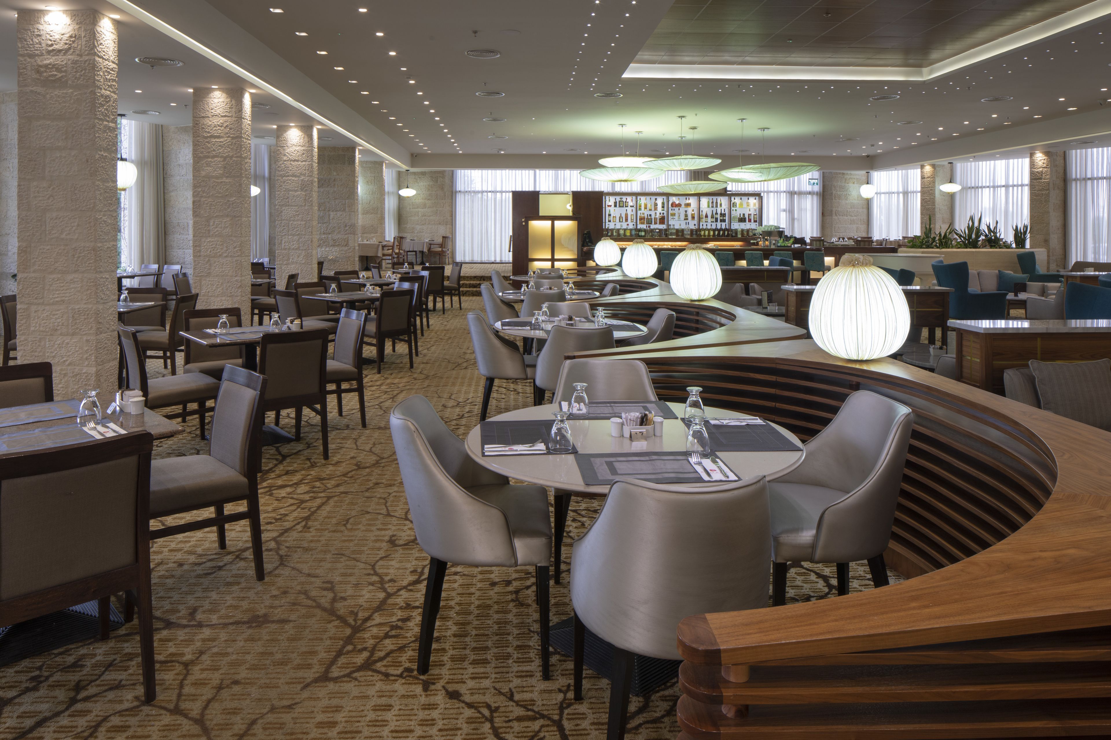 En moderne restaurant med runde borde, høje stole og et barområde.