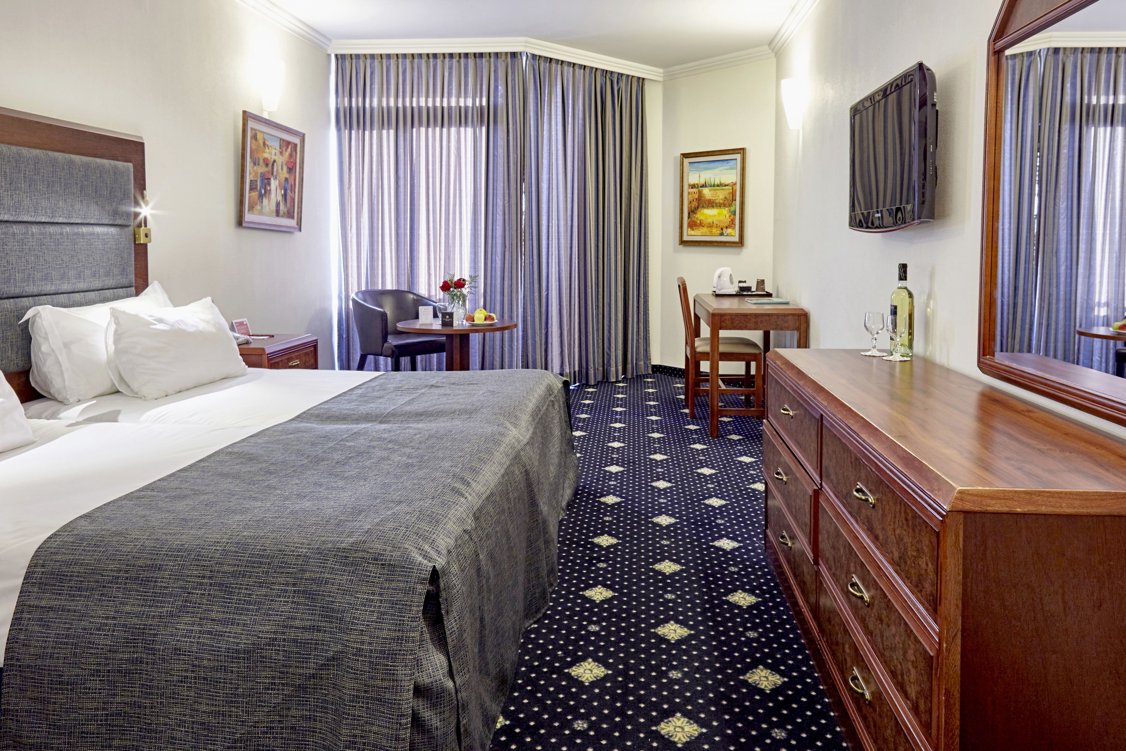 Une chambre d’hôtel avec un lit, un bureau, une chaise, une commode, une télévision et des rideaux.
