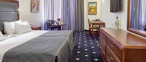 Une chambre d’hôtel avec un lit, un bureau, une chaise, une commode, une télévision et des rideaux.