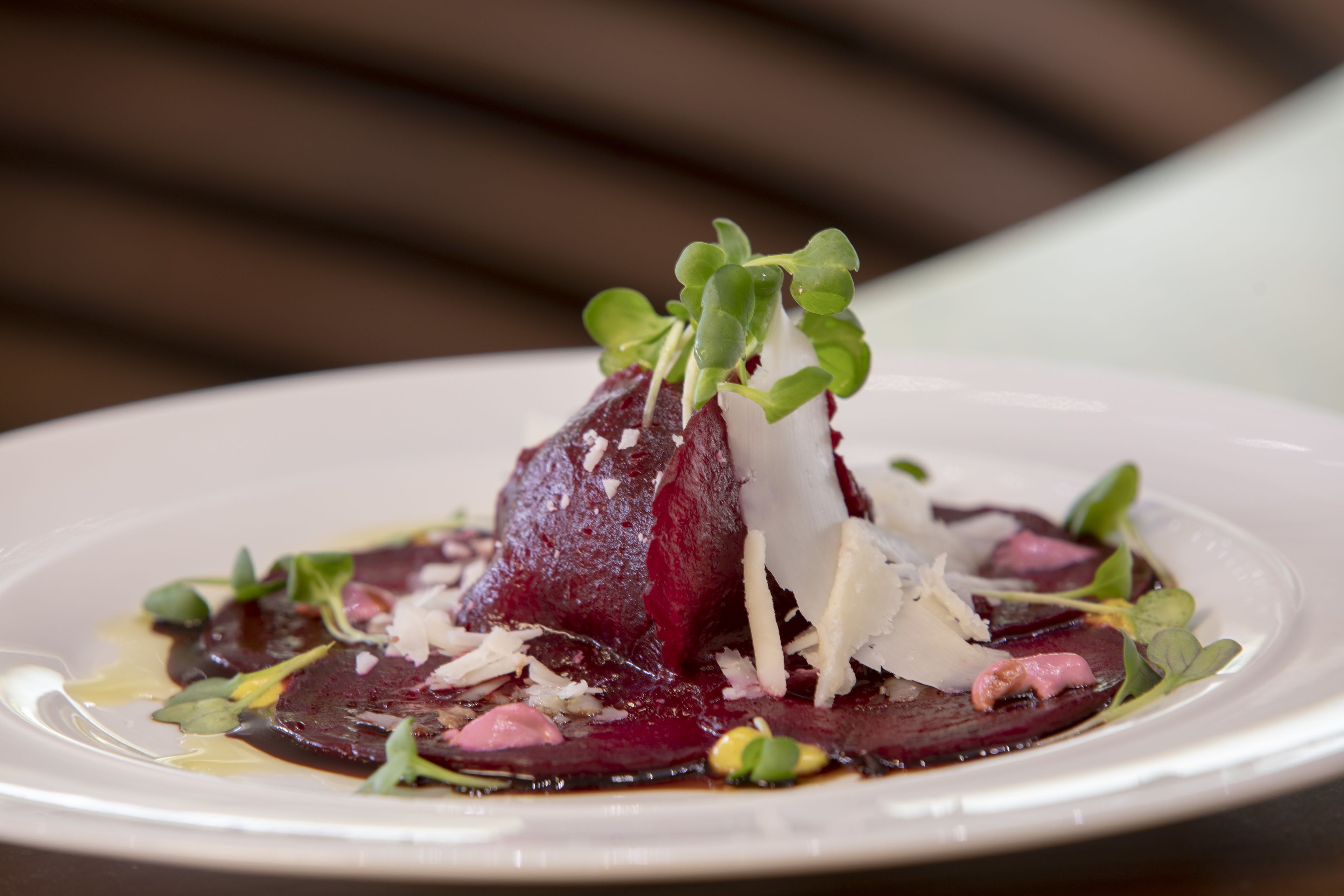 A plate of food with a beet centerpiece, garnished with greens and shaved cheese.