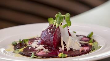 A plate of food with a beet centerpiece, garnished with greens and shaved cheese.