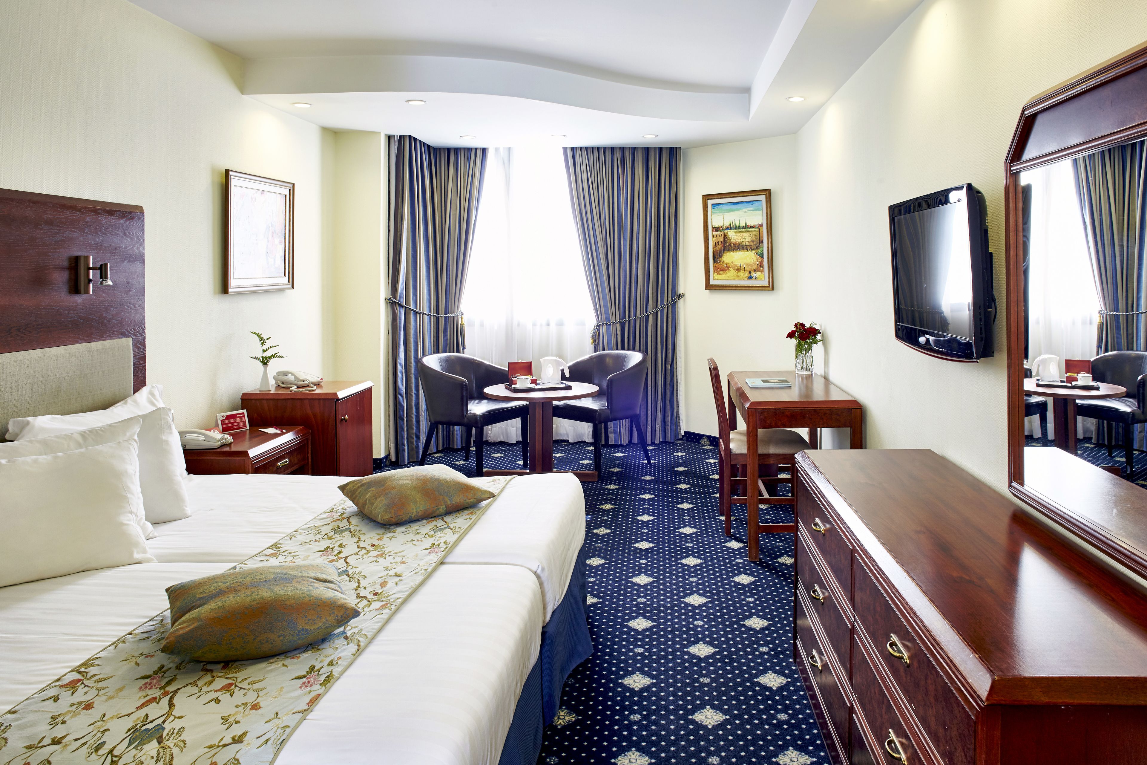 A hotel room with a bed, a desk, a chair, a dresser, a TV, and curtains.