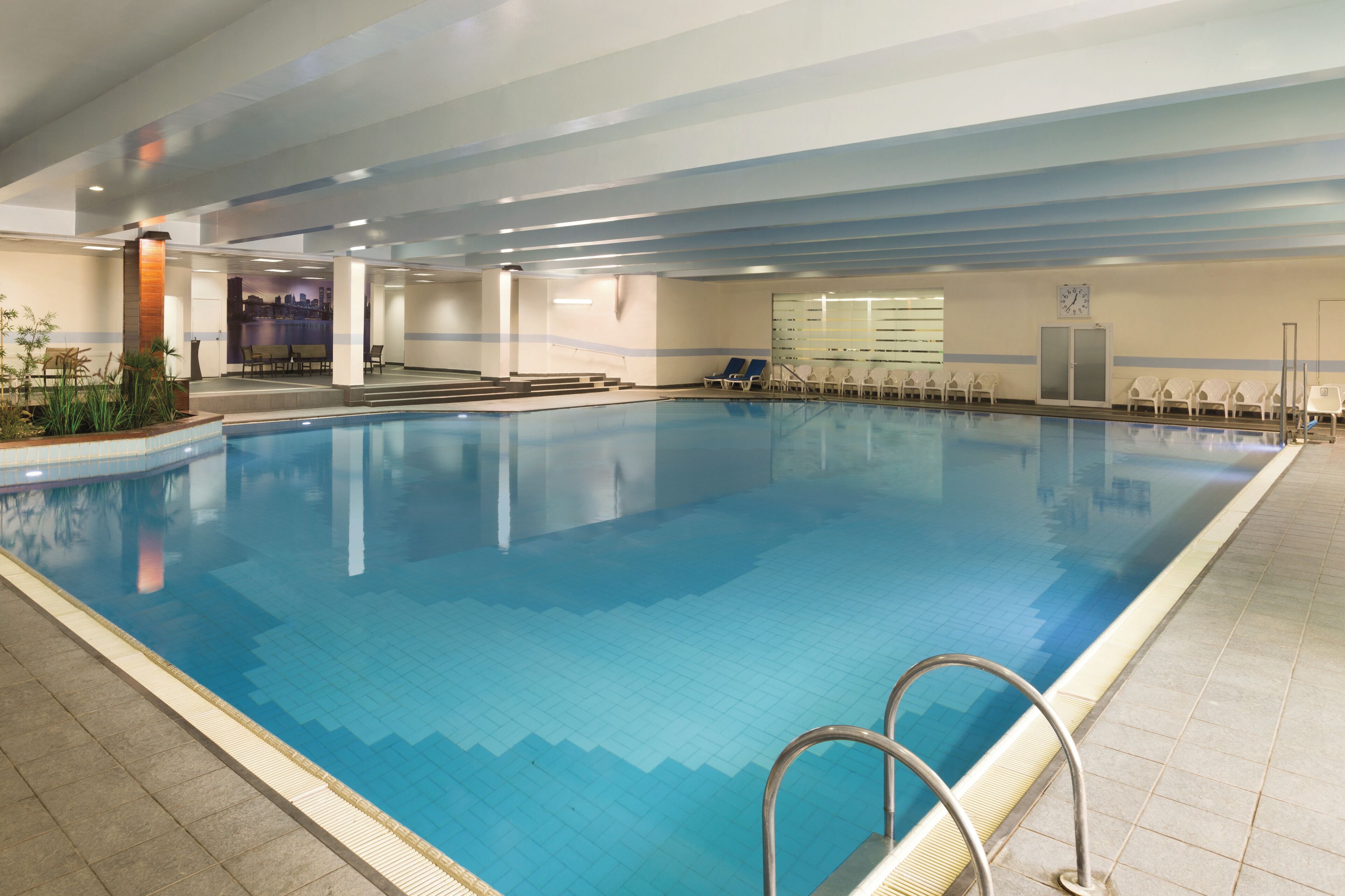 An indoor swimming pool with clear blue water, a tiled floor, and a metal pool ladder.