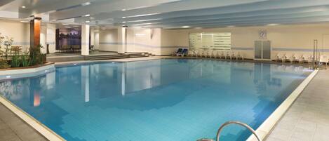 An indoor swimming pool with clear blue water, a tiled floor, and a metal pool ladder.