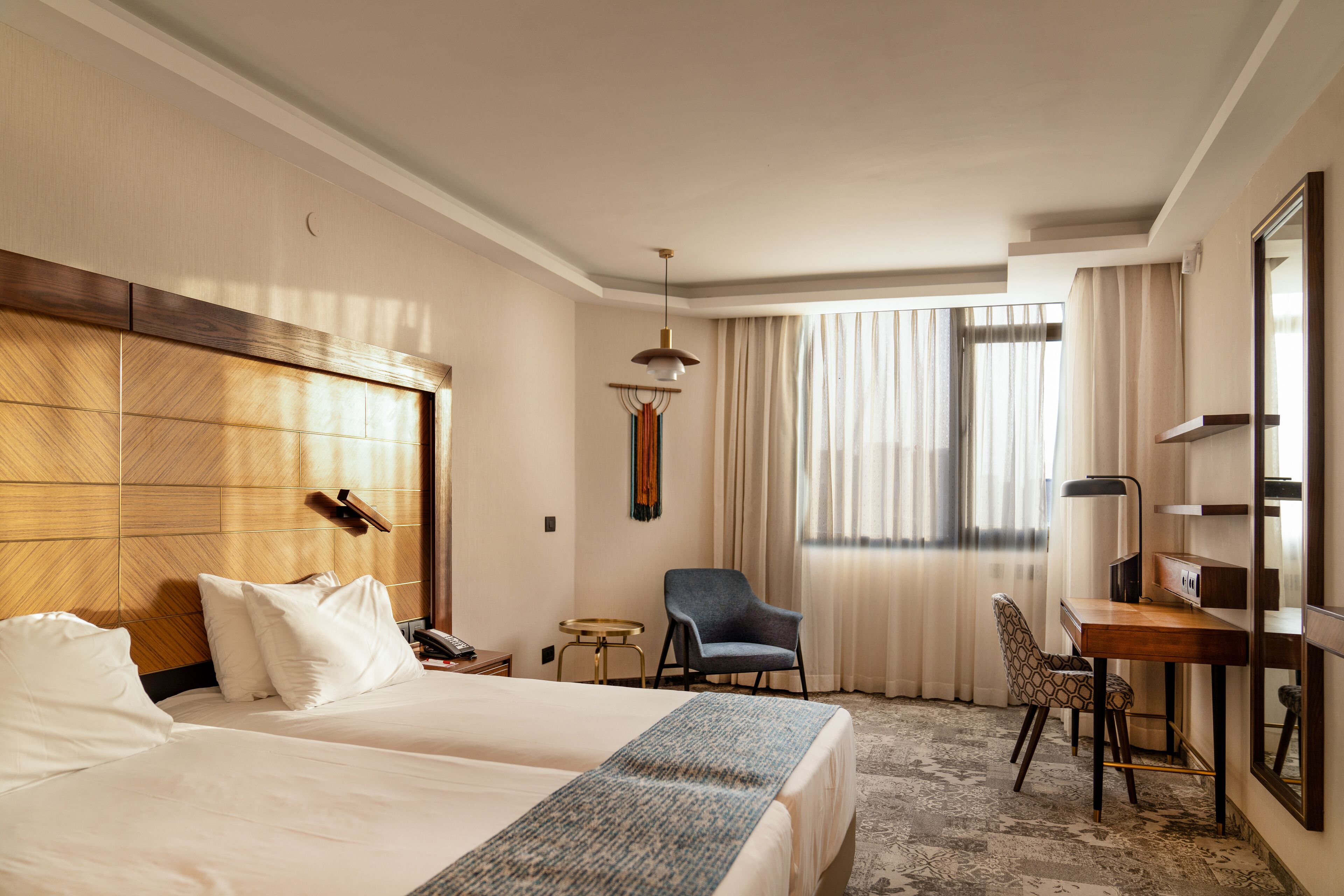 A hotel room with two beds, a desk, a chair, a lamp, and a large mirror.
