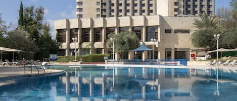 A hotel with a pool, a large building with balconies, and a clear blue sky.