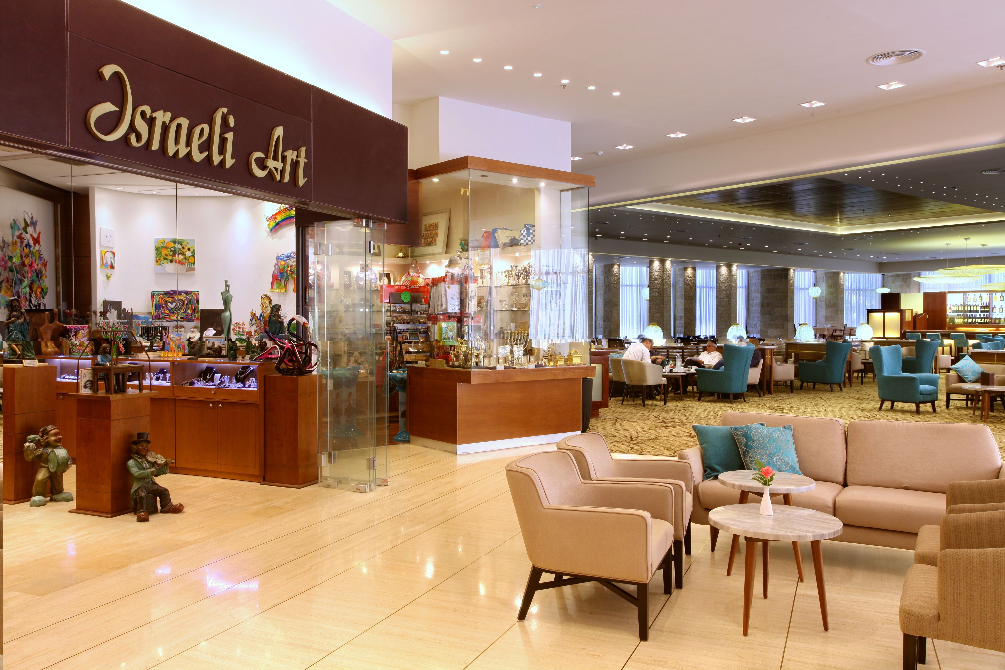A spacious lobby with a bar area, seating arrangements, and a store named 'Israeli Art'.