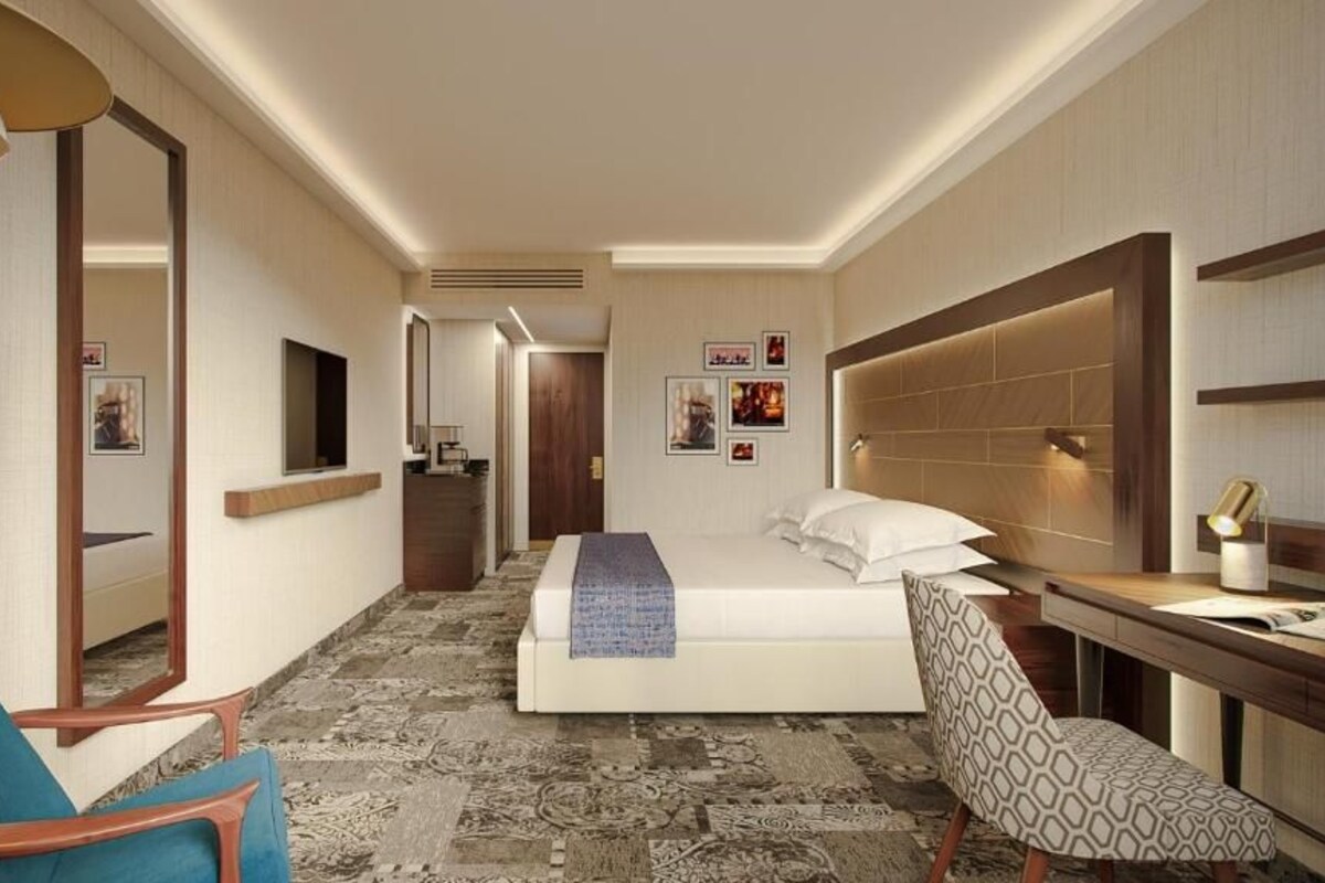 A hotel room with a bed, a desk, a chair, a mirror, and a television.