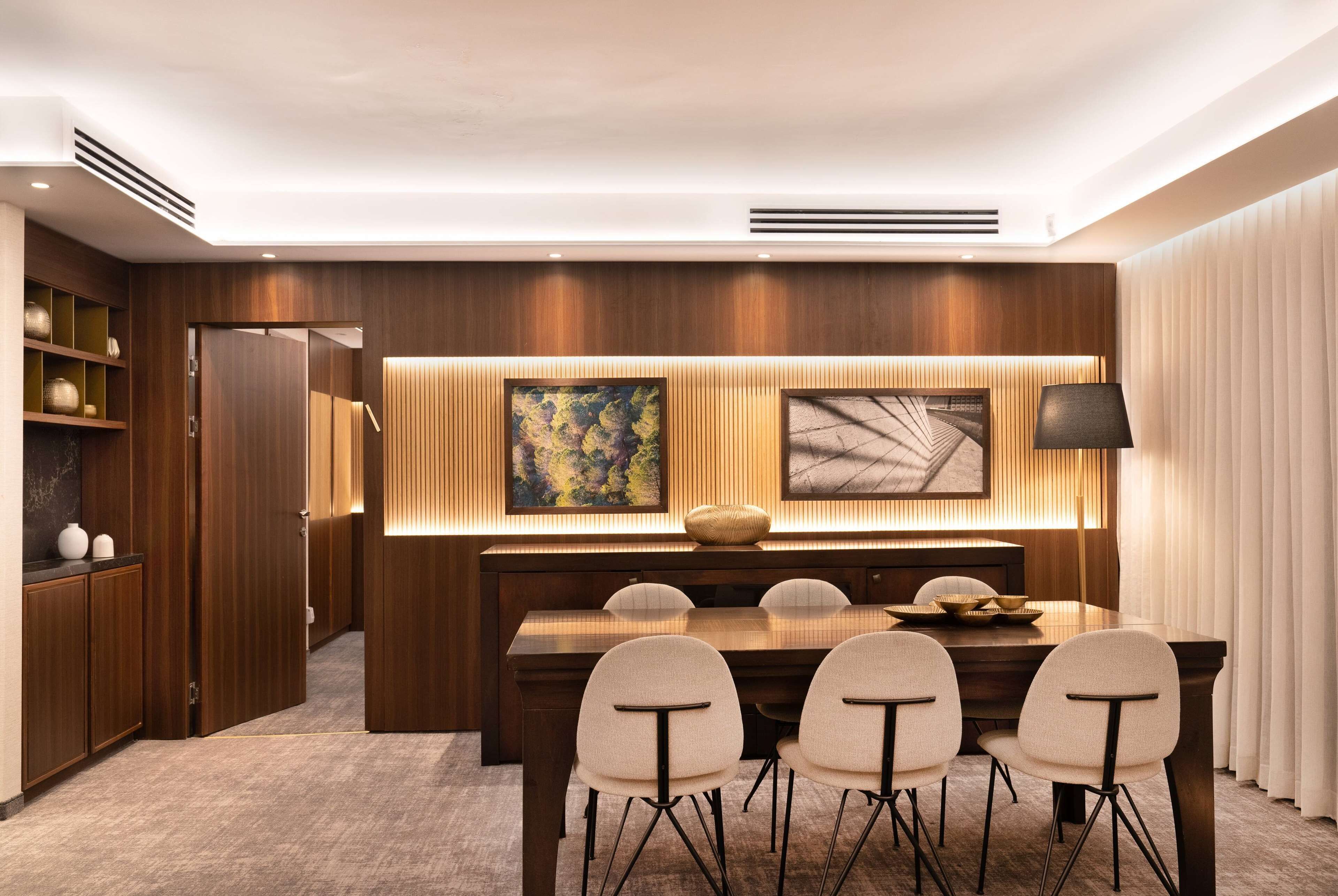 A modern dining area with a wooden table and chairs, a large painting, and a lamp.