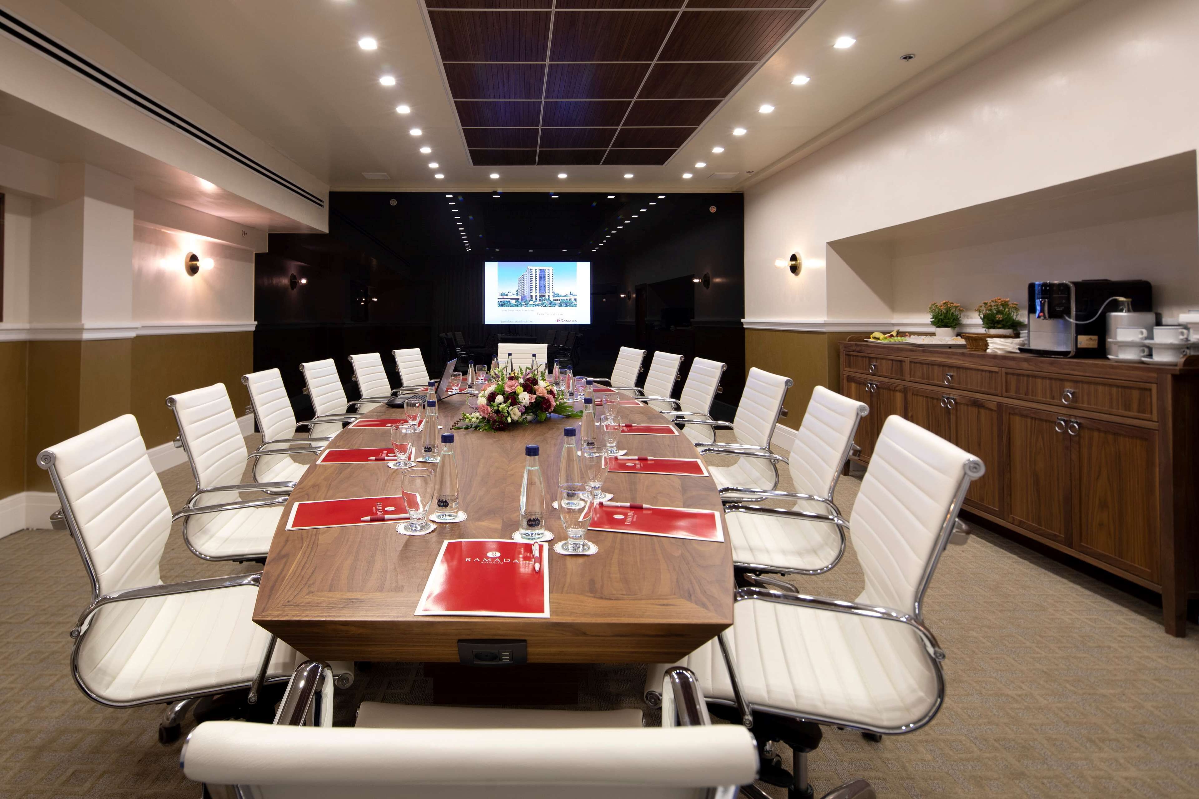 Una sala de conferencias con una larga mesa, sillas blancas, una pantalla de proyector y una estación de café.