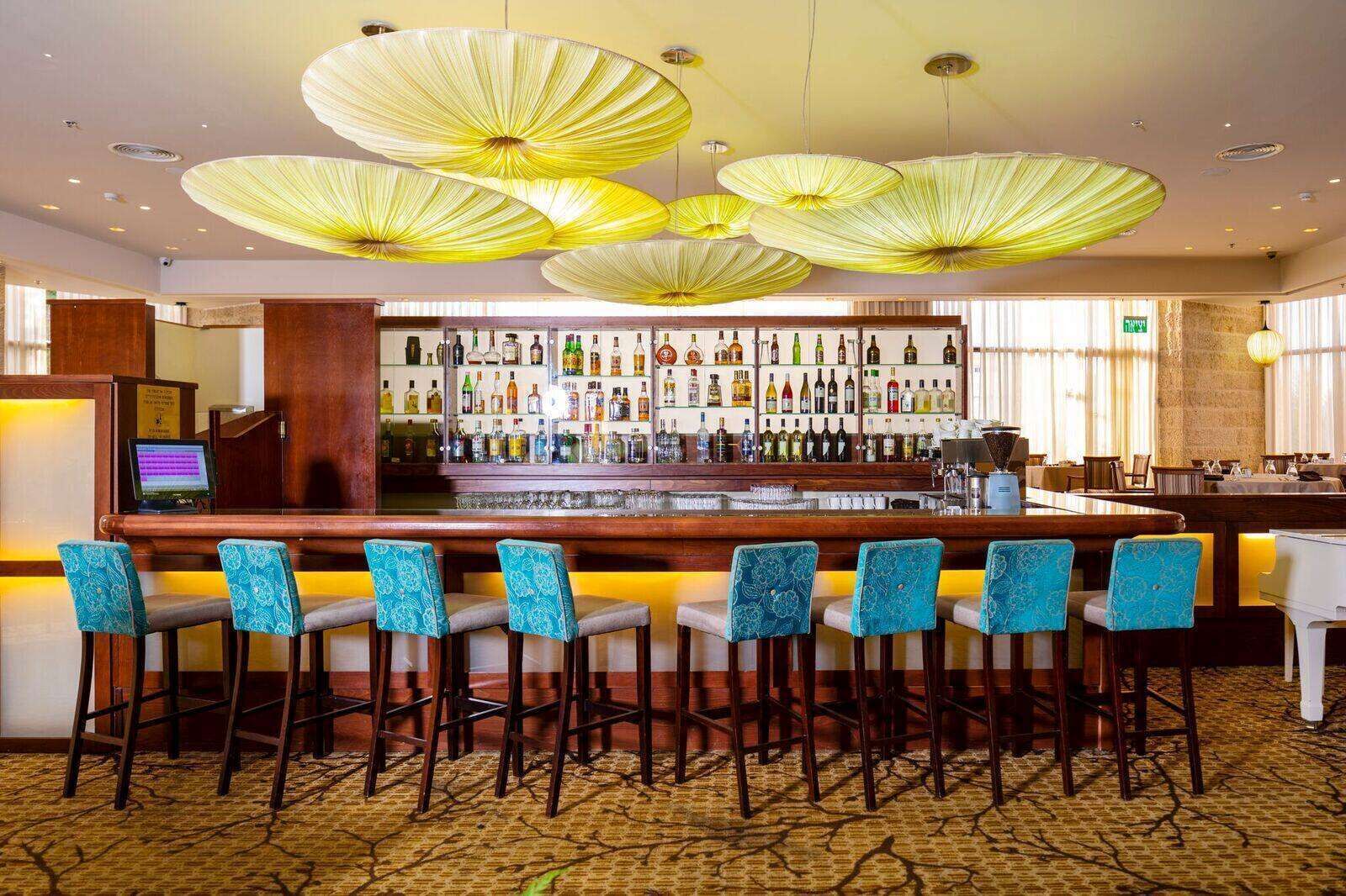 Un espace bar avec un comptoir en bois, de nombreuses bouteilles d’alcool et des tabourets de bar bleus à motifs.